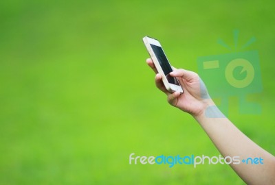 Hand Holding Smart Phone Against Green Grass Background Stock Photo