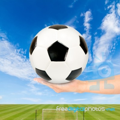 Hand Holding Soccer Ball With Soccer Field And Blue Sky Stock Photo