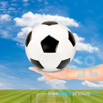 Hand Holding Soccer Ball With Soccer Field And Blue Sky Stock Photo