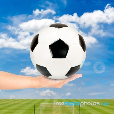 Hand Holding Soccer Ball With Soccer Field And Blue Sky Stock Photo