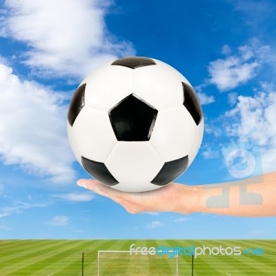 Hand Holding Soccer Ball With Soccer Field And Blue Sky Stock Photo