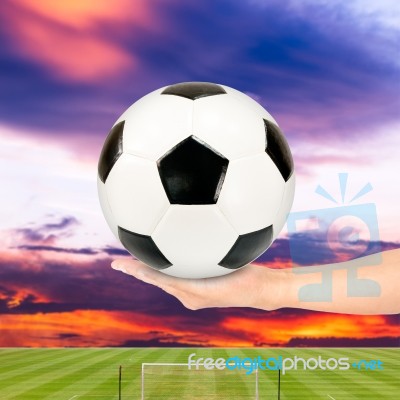 Hand Holding Soccer Ball With Soccer Field And Sunset Sky Stock Photo