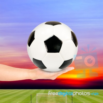 Hand Holding Soccer Ball With Soccer Field And Sunset Sky Stock Photo