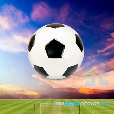 Hand Holding Soccer Ball With Soccer Field And Sunset Sky Stock Photo