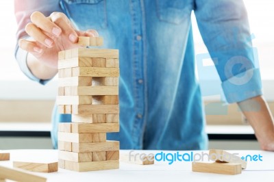 Hand Of Engineer Playing A Blocks Wood Tower Game (jenga) On Blu… Stock Photo