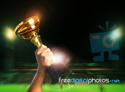 Hand Rising Soccer Football Championship Cup On Sport Competiton In Stadium Background Stock Photo