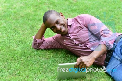 Handsome Man Lying On The Lawn With Tablet Stock Photo