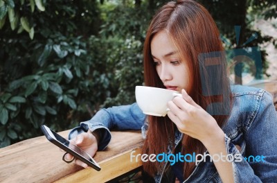 Happy Young Woman Drinking Coffee Outdoors And Using Smartphone Stock Photo