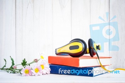 Headphones On Books With Flowers On White Wood Background Stock Photo