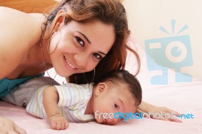 Hispanic Mom Lying Down On Bed And Holding Her Infant Son Stock Photo