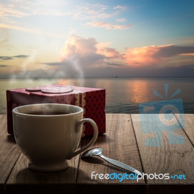 Hot Coffee And Gift Box On Wooden Table With Seascape Stock Photo