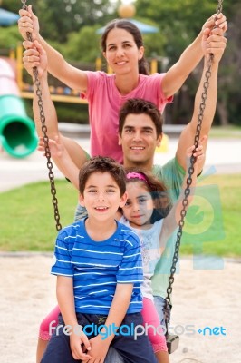 Jolly Caucasian Family Swinging In The Park Stock Photo