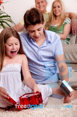 Kids Opening Christmas Gifts With Parents In The Background Stock Photo