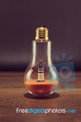 Lighthouse On Orange Sand In Spiral Bulb On Wooden Table Stock Photo