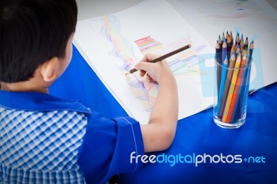 Little Asian Boy Sitting At The Table And Drawing By Colour Pencil Stock Photo