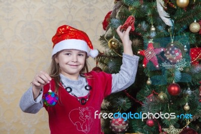 Little Girl In Santa Hat Near Christmas Tree Stock Photo