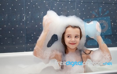 Little Girl Sitting In A Bath And Imposes Soap Suds On Her Head Stock Photo