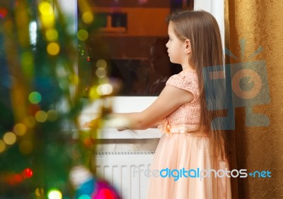 Little Girl Standing At The Window At Christmas Stock Photo