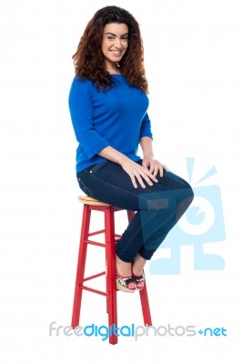 Long Curly Haired Lady Seated On Red Stool Stock Photo