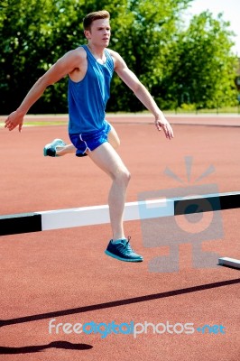 Male Athlete Jumping Hurdle Stock Photo