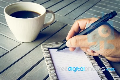 Man Hand With Pen Writing On Notebook. Coffee And Notebook On Wooden Table Stock Photo