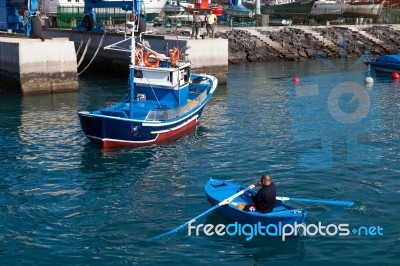 Man Rowing A Fishing Boat To Side Of Harbour In Tenerife Stock Photo