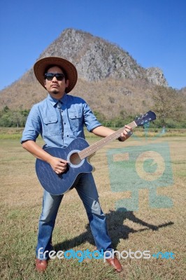 Man Standing And Playing Folk Guitar With Mountain Behind Stock Photo