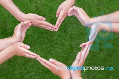 Many Arms Of Children Construct Heart Above Grass Stock Photo