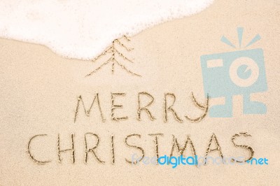 Merry Christmas Inscription On Wet Yellow Beach Sand Stock Photo