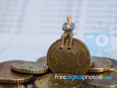 Miniature Businessman Sit On Euro Coins And Book Bank. Business Stock Photo