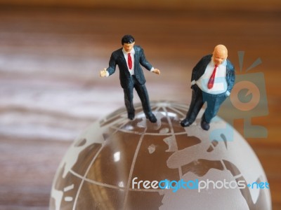 Miniature Businessman Stand On Globe Of Glass With Wooden Backgr… Stock Photo