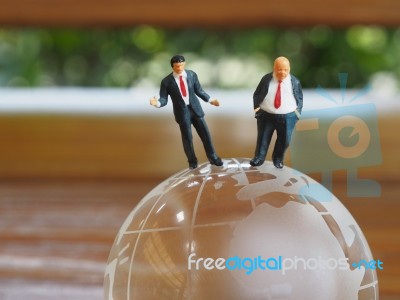 Miniature Businessman Stand On Globe Of Glass With Wooden Backgr… Stock Photo