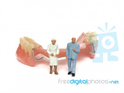 Miniature Elderly Couple Standing On Removable Denture, On White Background. Dental Health Concept Stock Photo