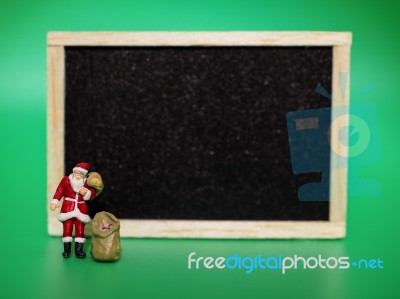 Miniature Santa Claus In Front Of A Blackboard On Green Backgrou… Stock Photo