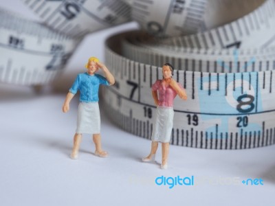 Miniature Woman Standing Near Measuring Tape, Thinking Of Weight… Stock Photo