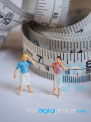 Miniature Woman Standing Near Measuring Tape, Thinking Of Weight… Stock Photo