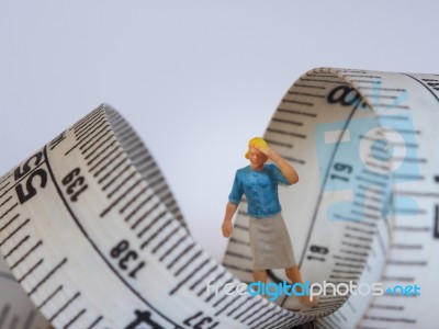 Miniature Woman Standing Near Measuring Tape, Thinking Of Weight… Stock Photo