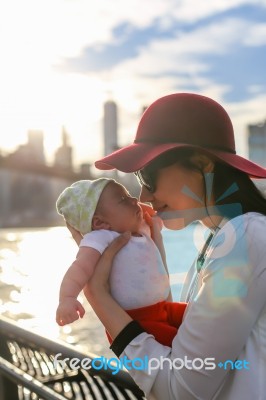 Mom Is Kissing Her Baby With The City In The Background Stock Photo