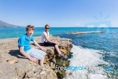 Mother And Son As Tourists Sitting On Rock At Blue Sea Stock Photo