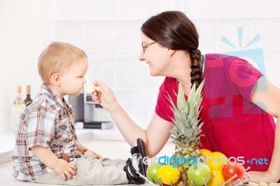 Mother Feeding Child In Kitchen Stock Photo