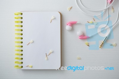 Notebook With Flowers And Earphones On White Desk Stock Photo