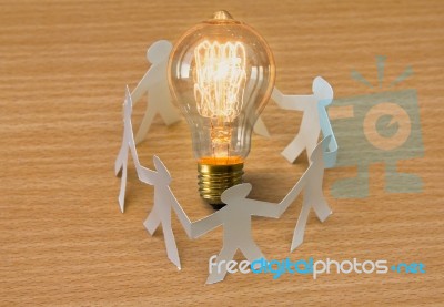 Paper Cut Of People Standing In A Circle Around Bulb Of Idea Stock Photo