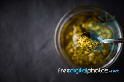 Pesto Sauce In The Metal Spoon With Blurred Jar Top View Stock Photo