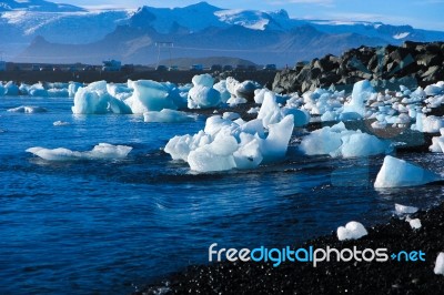 Pieces Of Ice On The Black Sand Beach In Iceland, With A Big Mountain Covered With Snow As A Background Stock Photo