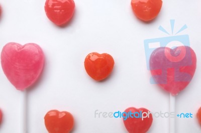 Pink Valentine's Day Heart Shape Lollipop With Small Red Candy In Cute Pattern On Empty White Paper Background. Love Concept. Colorful Hipster Style. Knolling Top View Stock Photo