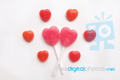 Pink Valentine's Day Heart Shape Lollipop With Small Red Candy In Cute Pattern On Empty White Paper Background. Love Concept. Colorful Hipster Style. Knolling Top View Stock Photo