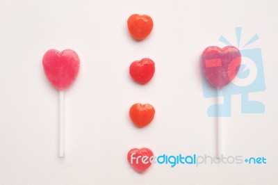 Pink Valentine's Day Heart Shape Lollipop With Small Red Candy In Cute Pattern On Empty White Paper Background. Love Concept. Colorful Hipster Style. Knolling Top View Stock Photo