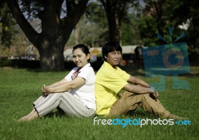 Portrait Of Beautiful Couple Sitting On Ground In Park Stock Photo