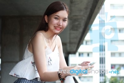 Portrait Of Thai Adult Beautiful Girl Using Her Smart Phone And Smile Stock Photo