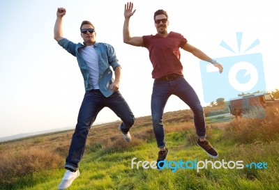 Portrait Of Two Friends Jumping In Field Stock Photo